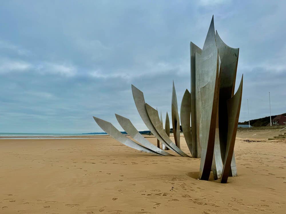 Metal sculpture that resembles wings rises out of a sandy beach.