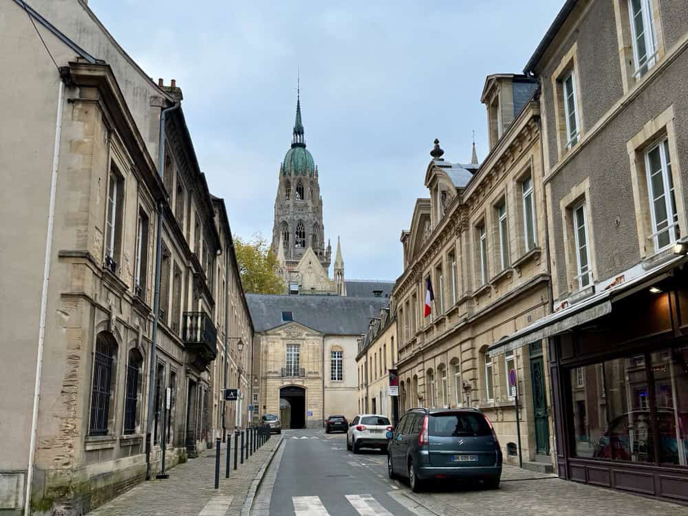 Street scene in Bayeux France with a cathedral spire in the background.