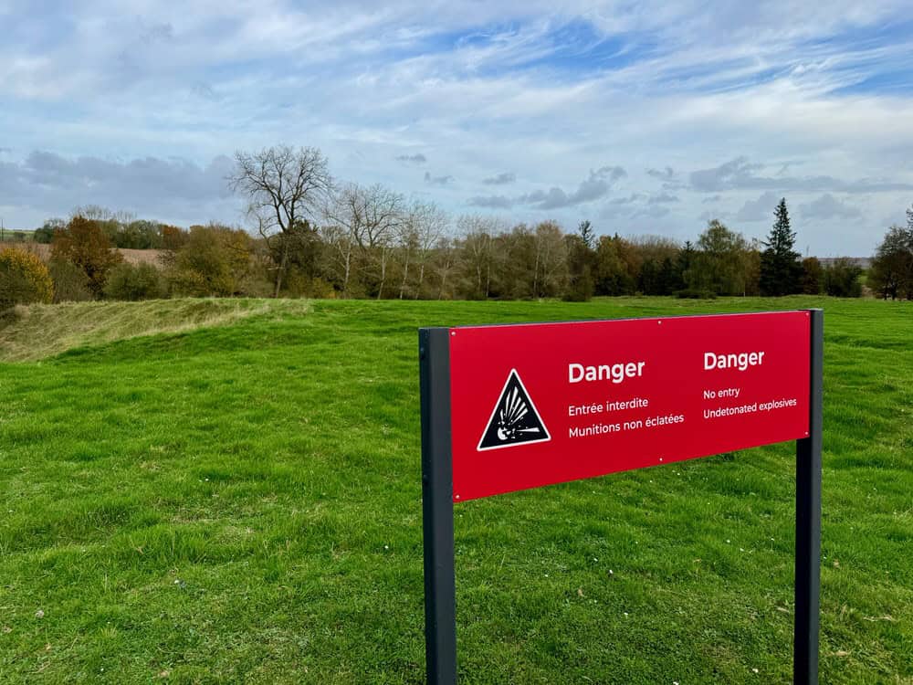 A sign in front of a grassy expanse warning against undetonated explosives.