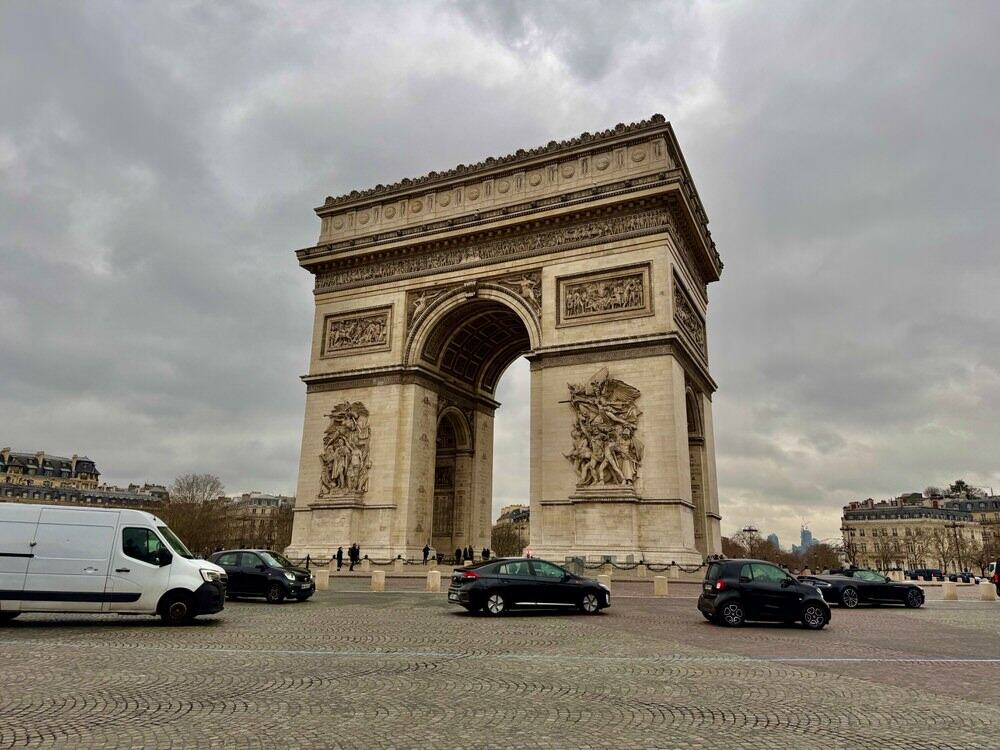 Large stone triumphal arch stands in the center of a busy traffic circle