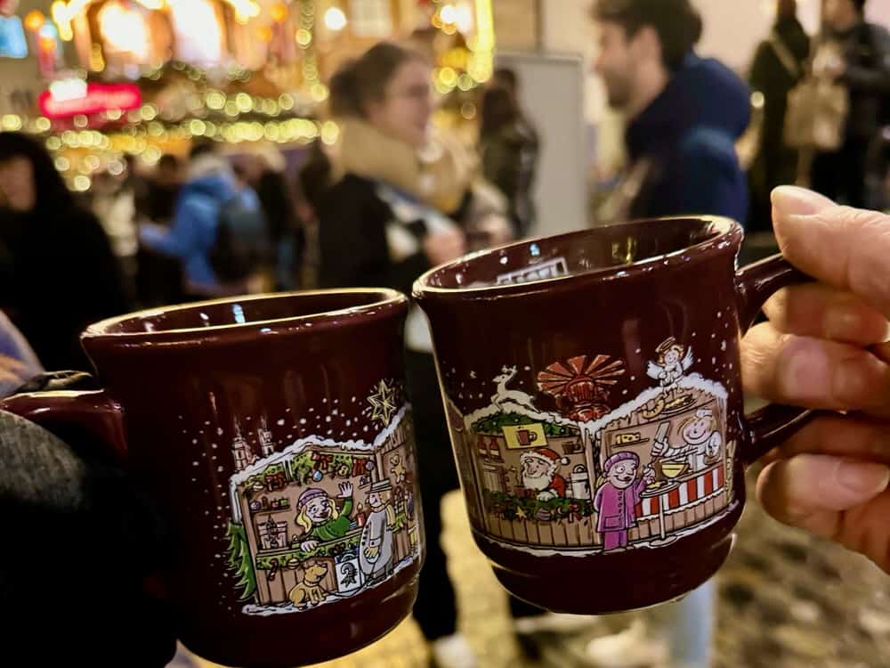 People cheers two mugs full of gluhwein in a busy Christmas market