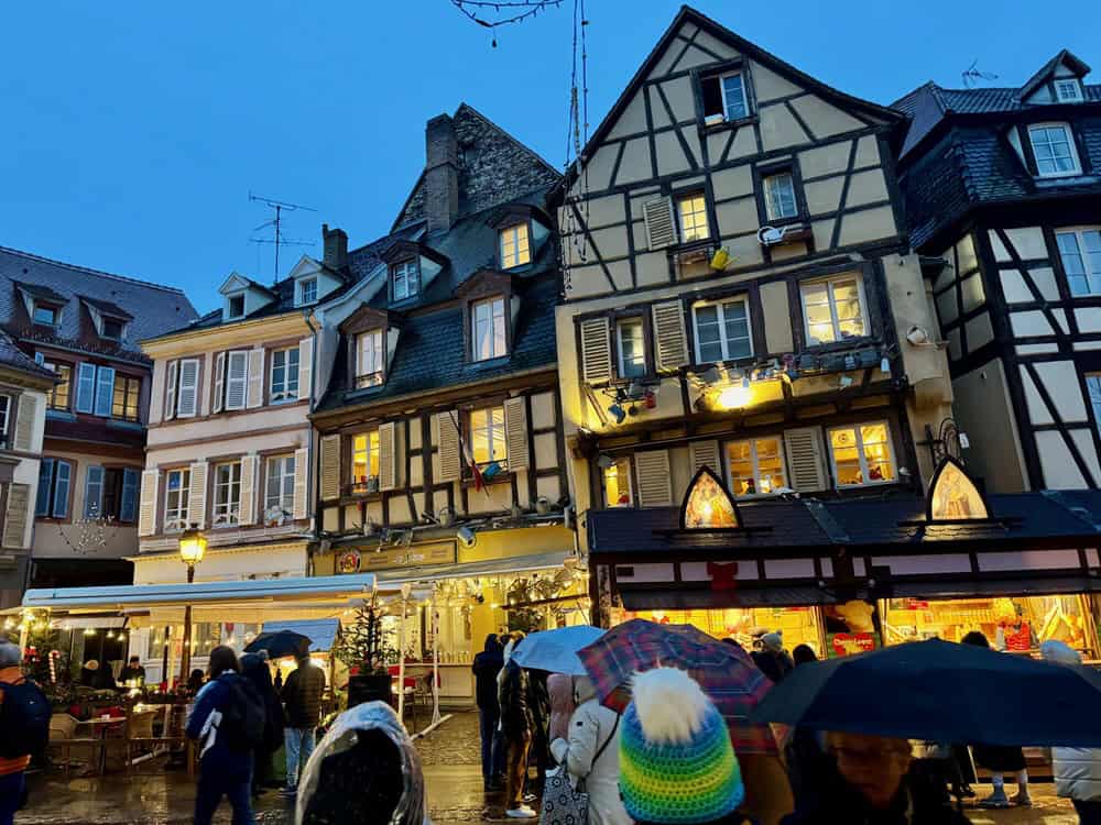 Half timbered house in Colmar France at dusk with Christmas market stalls in front of them.