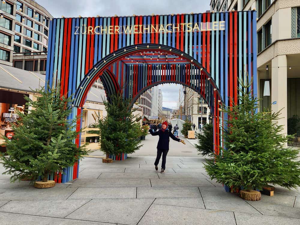 Woman poses in front of a colorful entrance to a Zurich Christmas market