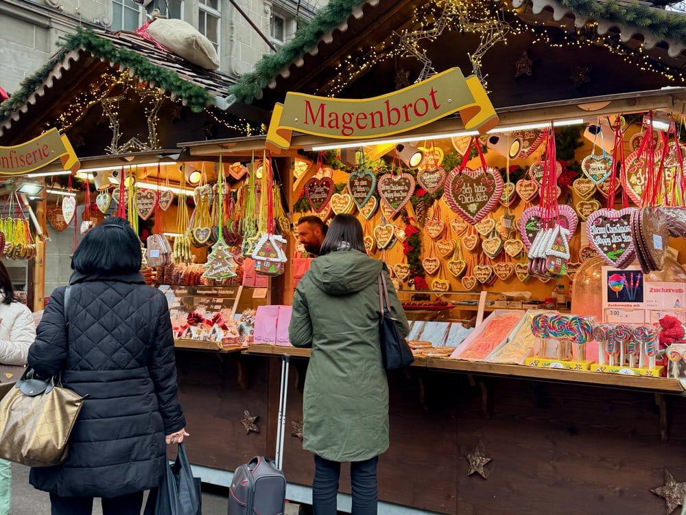 Women stand in front of a cookie stand at a Christmas market with hanging gingerbread hearts