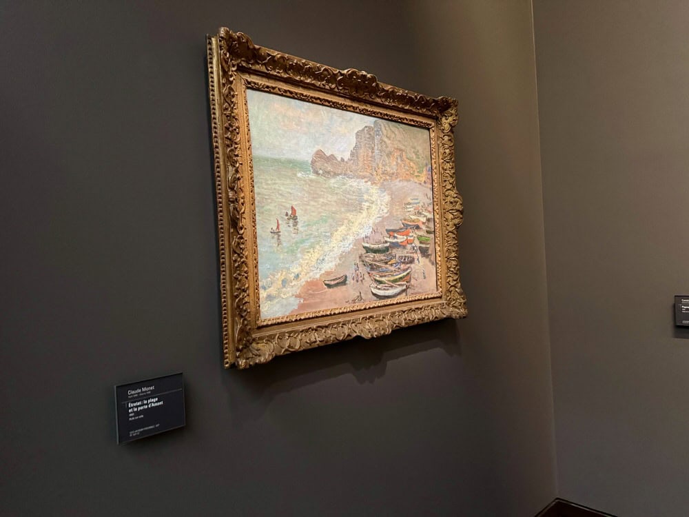 A framed Claude Monet oil painting of Etretat France hanging on a museum wall.