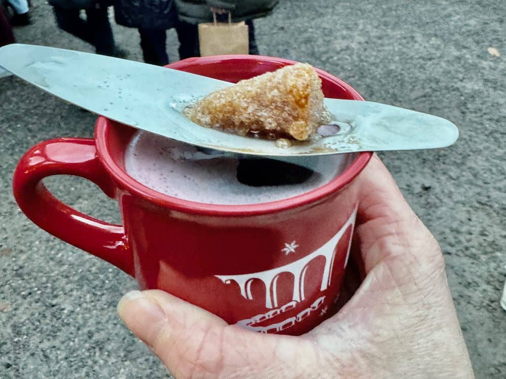 A hand holds a Christmas market mug filled with gluhwein with a sugar cube melting into it.