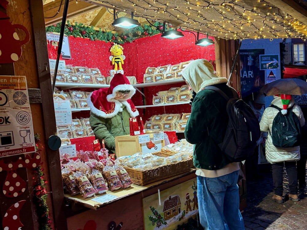Woman wearing a Mrs. Claus hood sells loaves of pain d'epices at a French Christmas market.