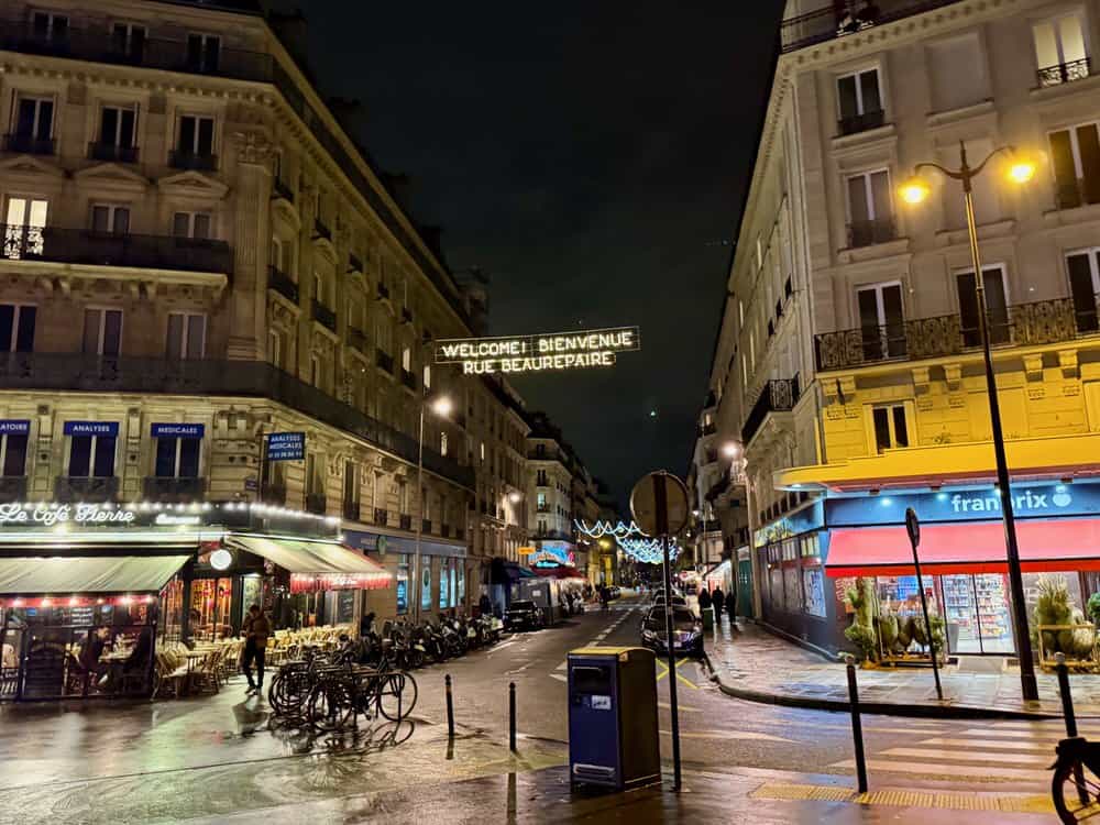 Brightly lit cafes and store fronts in a Paris neighborhood at night.