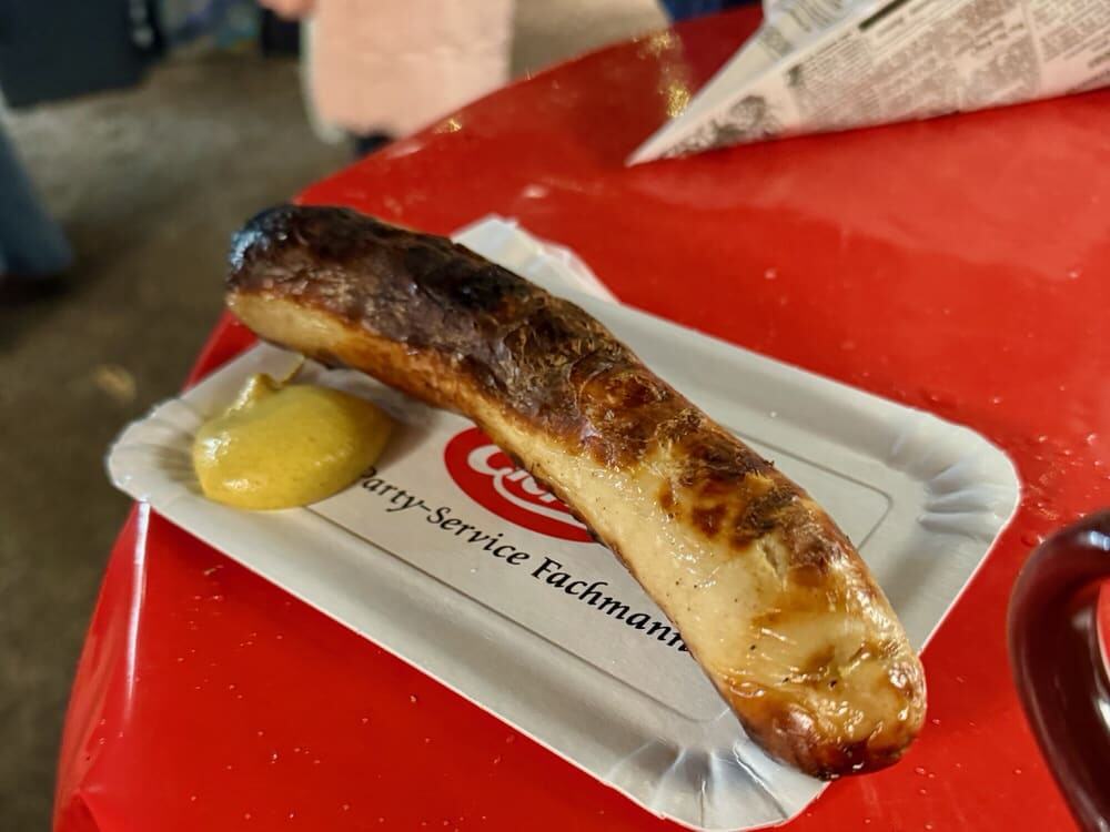 A grilled sausage with mustard on a paper plate.