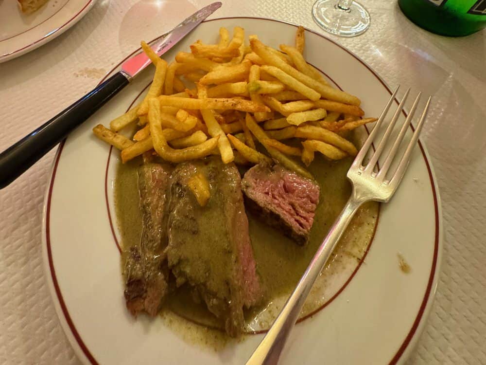 A plate of french fried potatoes and flank steak covered with a brown steak sauce.