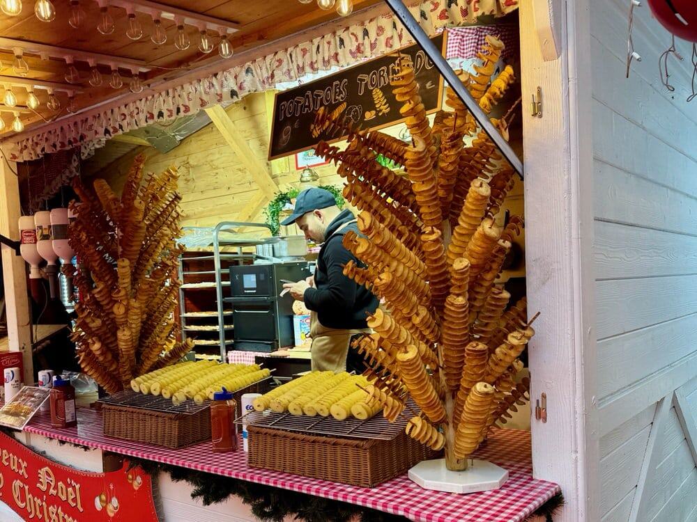 Man works in a fully stocked potato tornado stand at a Paris Christmas market
