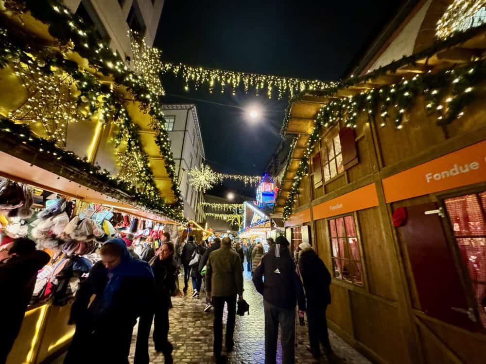 People mill among the stalls and lights of the Basel Christmas market