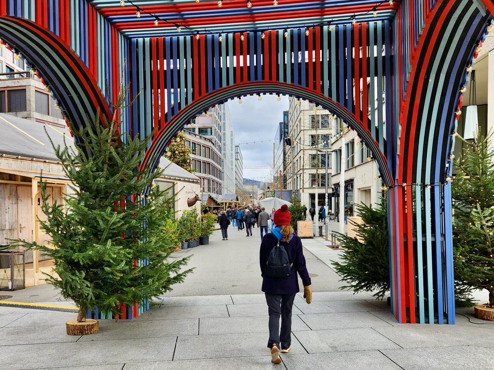 Woman walks through a colorful archway into a Zurich, Switzerland towards a Christmas market