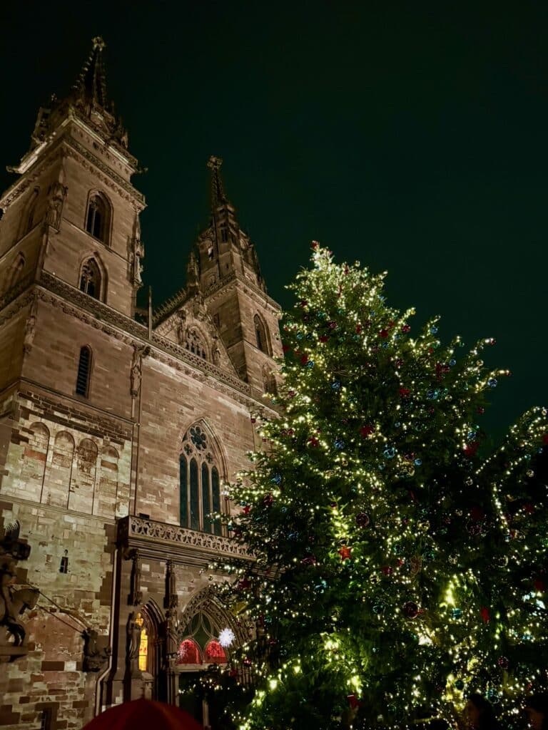 Outside of a large stone cathedral in Switzerland with a brightly decorated Christmas tree in front