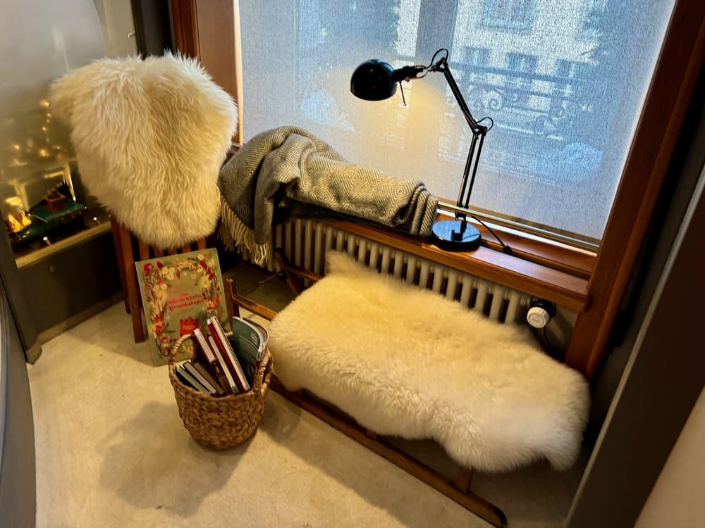 Corner of a room decorated with plush covers and blankets and a bright lamp for reading.