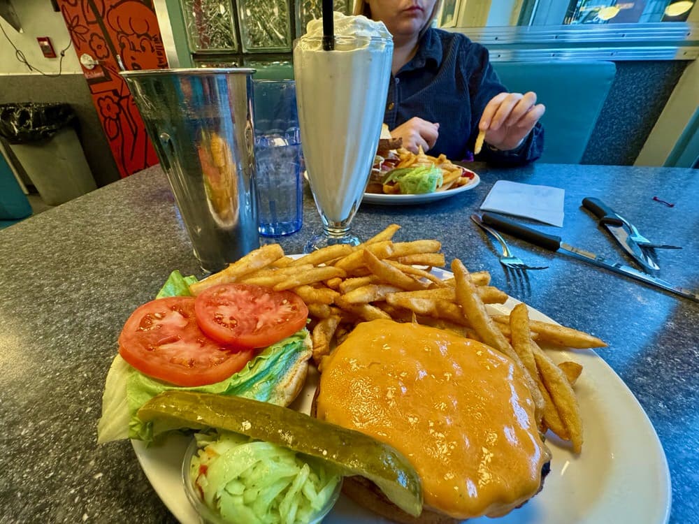 A plate covered with a cheese burger and fries with a vanilla milkshake on a dinner table at Zaks diner