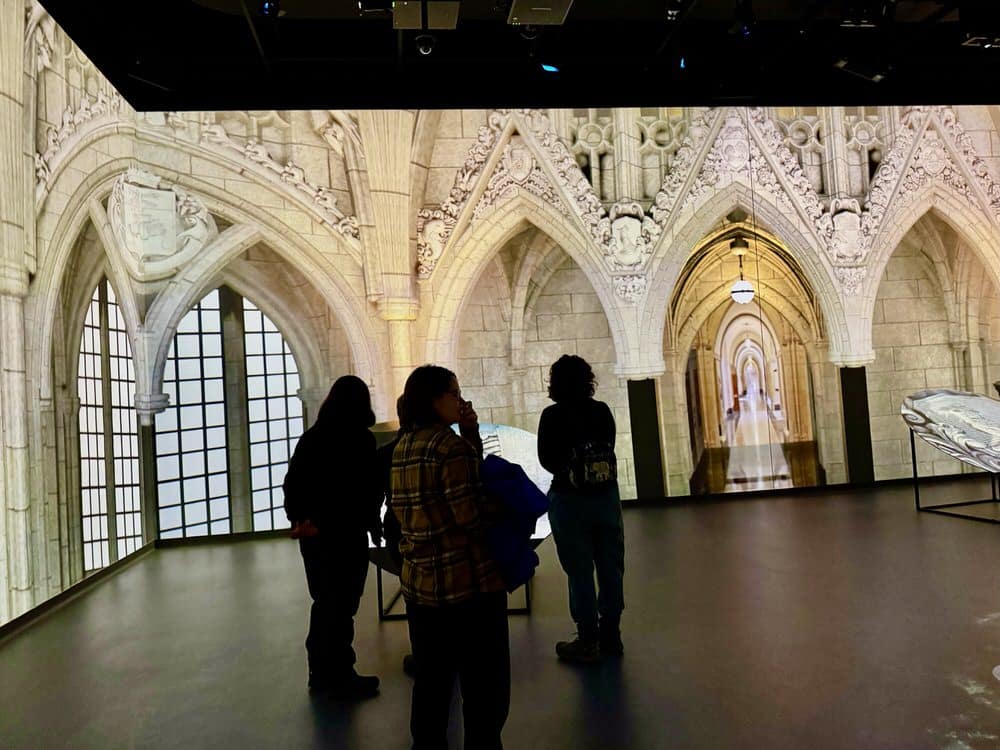 Three guests stand in front of video projects of Canada's centre block parliament building interior in the Parliament Immersive Exhibit