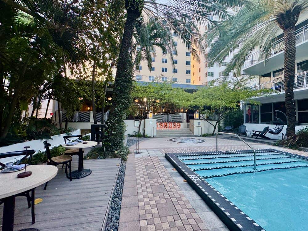 Tables and palm trees surround a pool on the backside of National Hotel Miami Beach