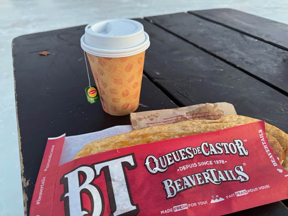 A Beavertail pastry and a hot tea rest on the top of an outside picnic table