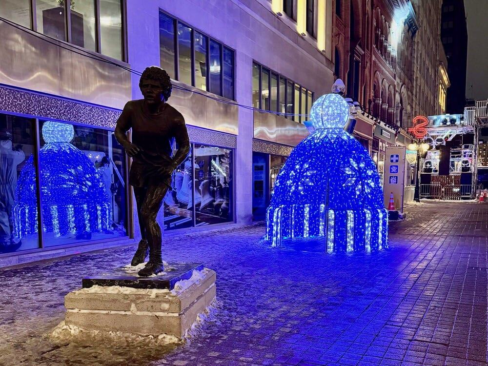 Statue of Terry Fox running his trans-Canadian marathon on Sparks street at night near a light display of a toque hat.