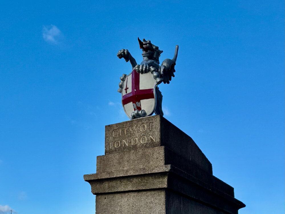 A silver dragon holding the English coat of arms stands a top a pillar labeled "City of London"