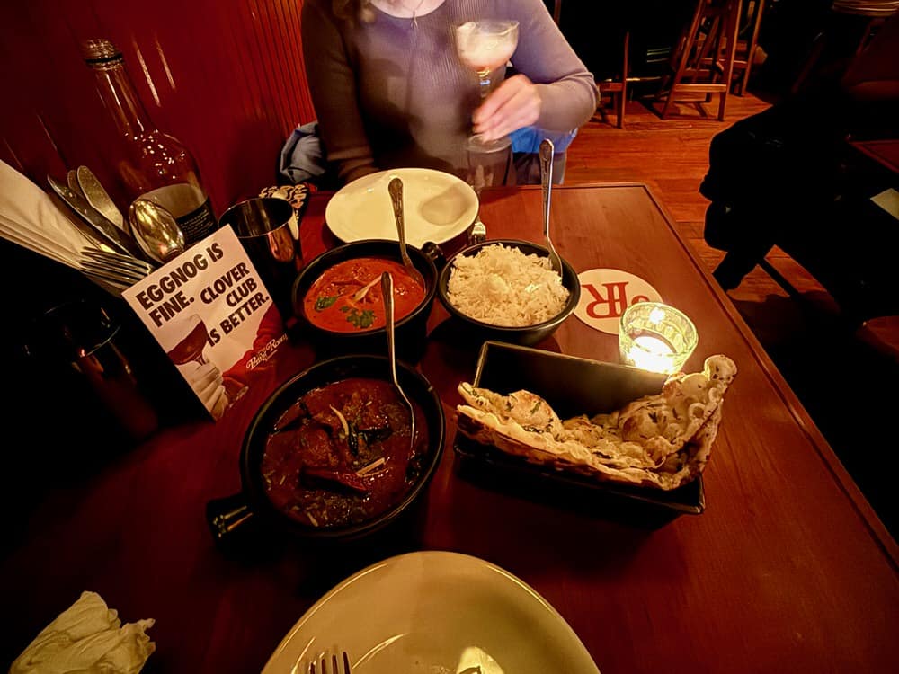 Several small dishes of Indian food including rice, naan, and curry sit in front of diners at a restaurant