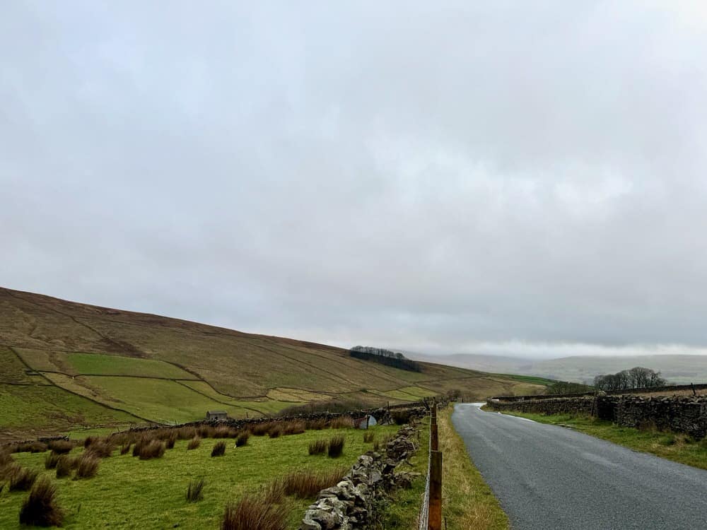 A road winds through the Yorkshire Dales on an overcast day.