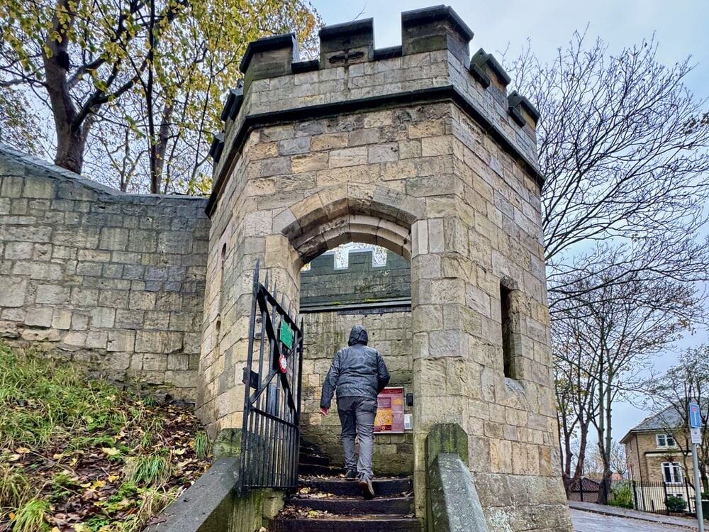 Man hikes up steps to the top of the stone medieval walls surrounding York City Centre