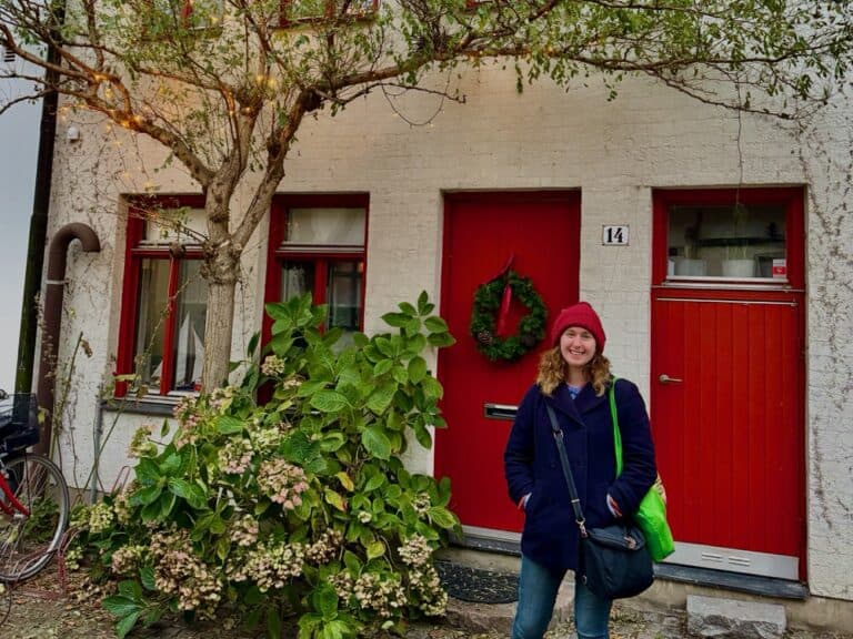 Woman in winter wear stands in front of two red doors and a tree decorated with Christmas lights in southern Sweden