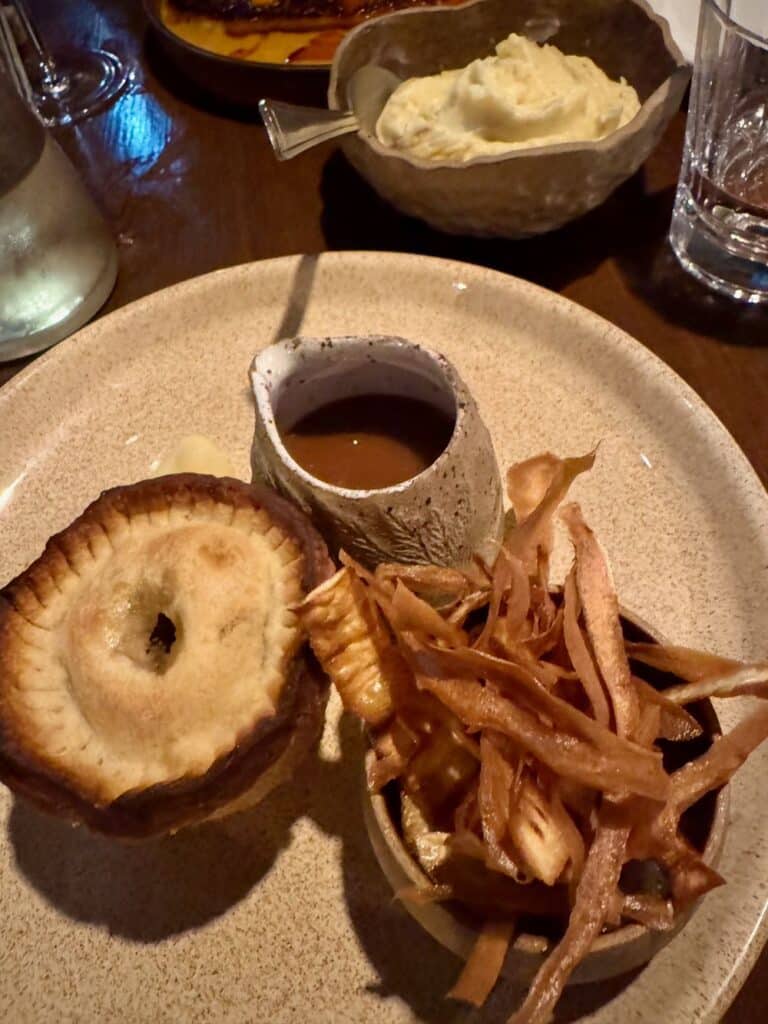 A handmade dinner pie with gravy and side of mash and french fried onions