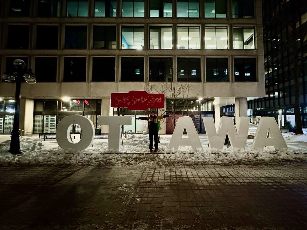 Woman forms the second T in Ottawa with her body in an Ottawa sign snow sculpture.