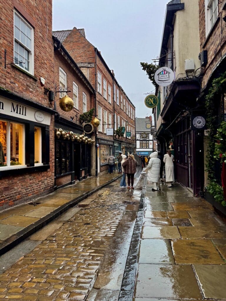 Rain falls on the far end of the Shambles, a short cobblestone shopping street in York with medieval and Tudor buildings
