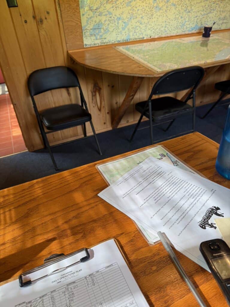 An office desk strewn with papers and a BWCAW map posted on a wall.