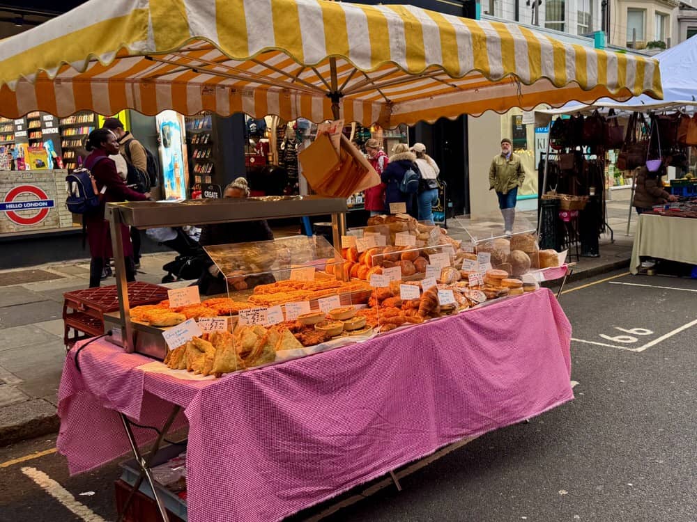 A booth filled with baked goods including samosas, quiches, and breads on the Portobello Road market