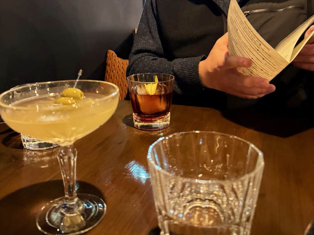 Various glasses including one containing whisky and one holding a gin martini sit on a restaurant table.