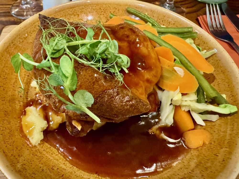 Plate of pub food include vegetables and Yorkshire pudding with pork sausages at an English pub