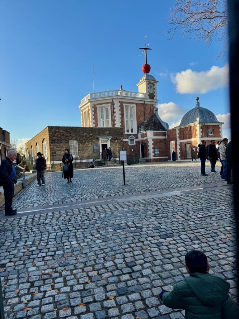 People in the courtyard of the Royal Observatory London next to the Prime Meridian marker