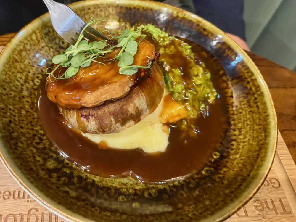 A plate of traditional British food included mashed potatoes, mushy peas, and a steak and ale pie covered with gravy.
