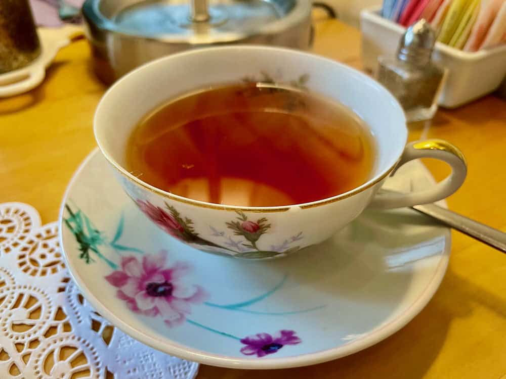 A full brewed cup of tea in a floral pattern china cup and saucer with a spoon on the side.