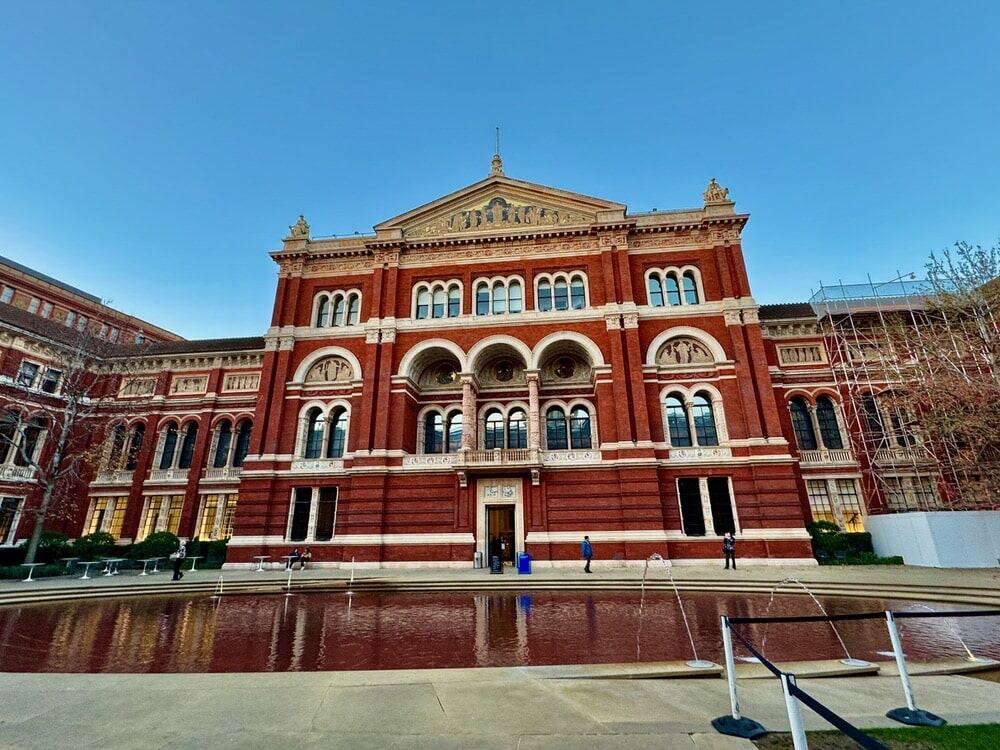 Red brick Victorian museum facade sits behind a large sunken fountain.