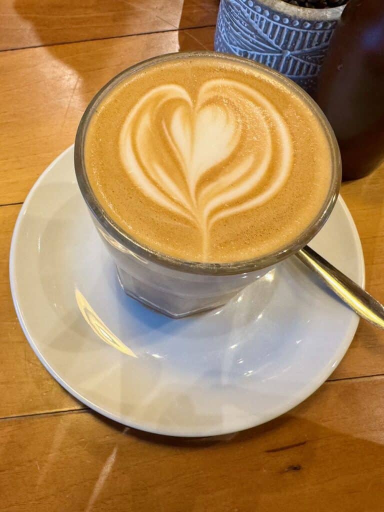 A full glass holding a coffee beverage with a heart in the milk foam.