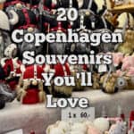 A Christmas market booth stuffed full of nisse figurines (gnomes) of various sizes and colors. Text overlay reads "20 Copenhagen Souvenirs You'll Love"