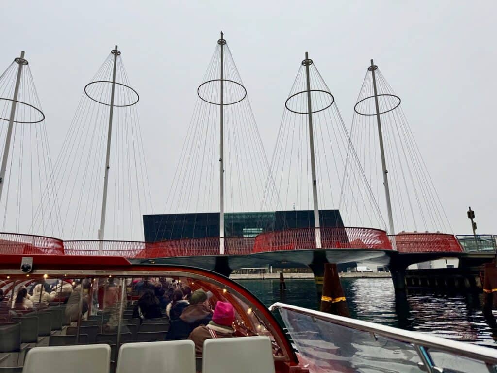 A canal cruise boat noses under a distinctive pedestrian bridge over a Copenhagen canal.
