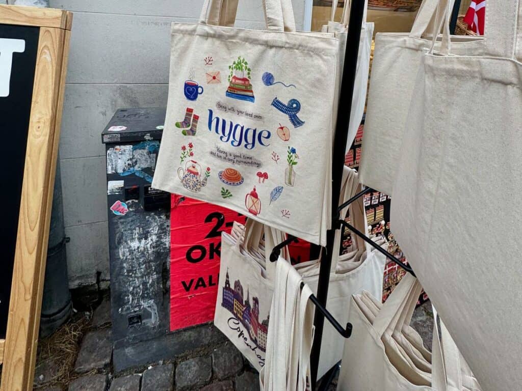 Cotton tote bags with hygge inspired graphics and Copenhagen city scenes hang from an outside rack.