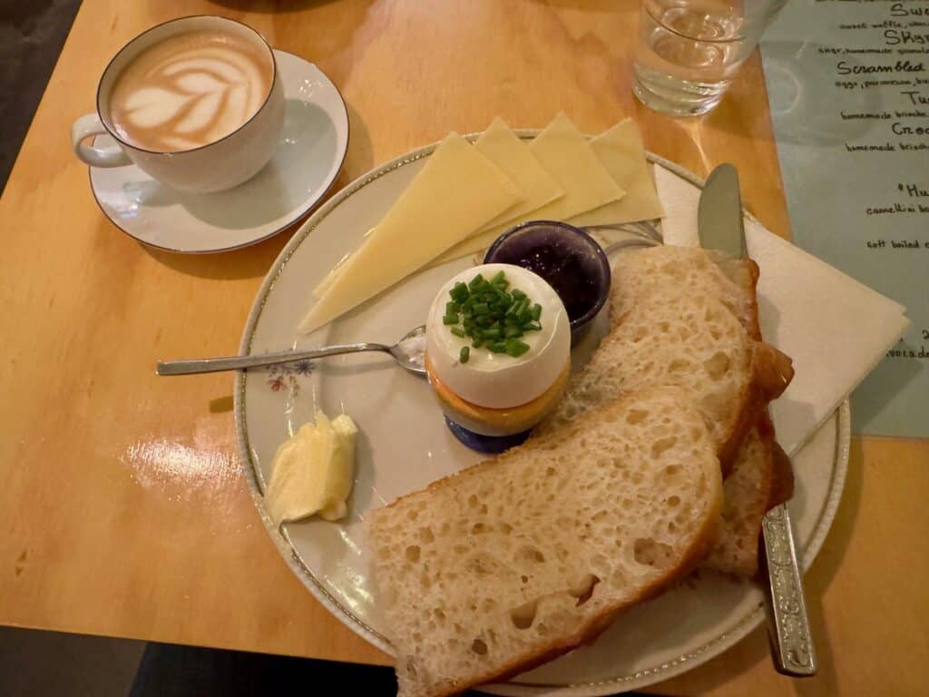 View of breakfast featuring a coffee drink in a mug and sauce and a plate of a soft boil egg, sliced bread, and cheese.