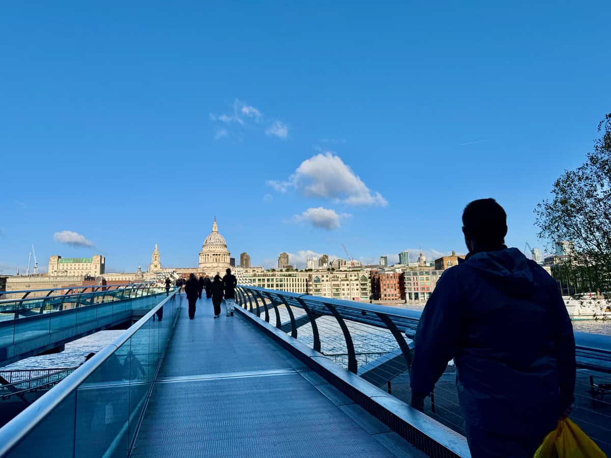 A man holding a shopping bag walks towards St. Paul's Cathedral in the City of London via the Millennium Bridge pedestrian bridge across the Thames River