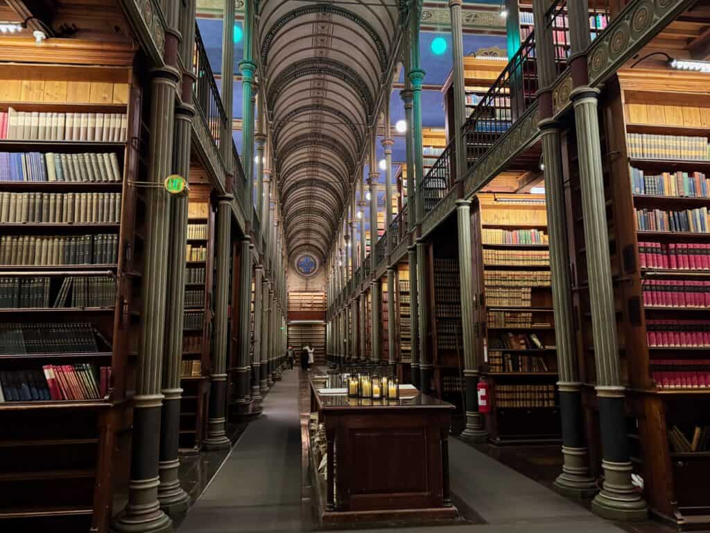 Looking down the center aisle of a historic European university library lit by sconces.