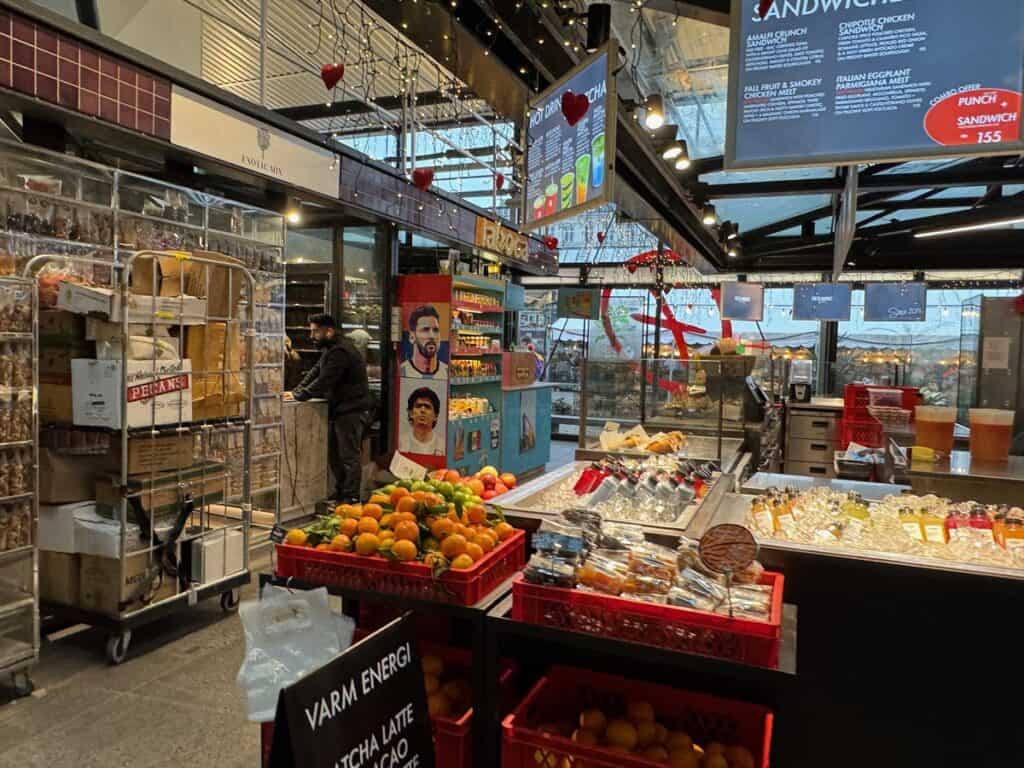Booths selling produce, juice and other food items inside a covered food market