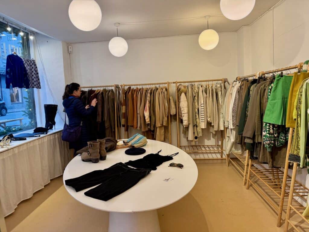 Woman rifles through color coded clothing racks inside a Copenhagen secound hand clothing shop.