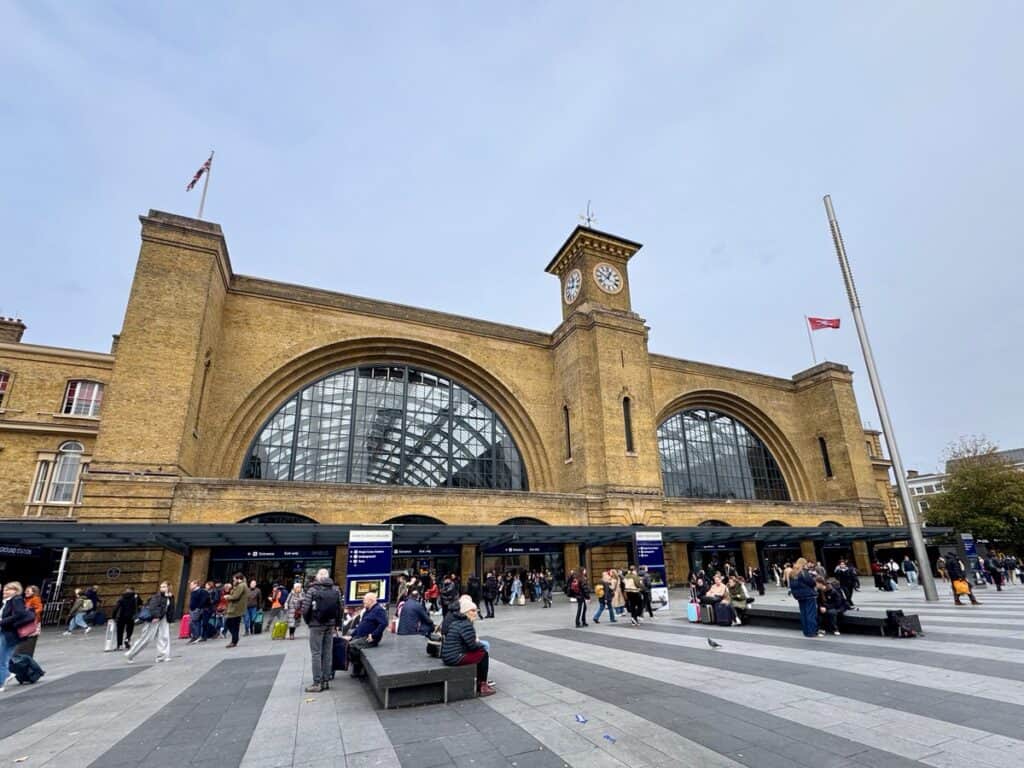 Travelers mill outside of a large brick train station in central London.